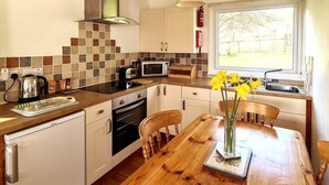 A compact kitchen with a wooden table, a microwave, a kettle, and a window with a view of greenery. - Ta Mill Holidays - Meadowview Chalet 3 (Launceston)