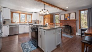 Una cocina amplia con armarios blancos, una isla central, una chimenea y un comedor con mesa y sillas.