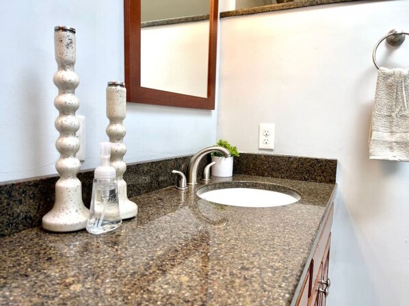 Un baño con encimera de granito, un lavabo blanco, un espejo y dos saleros y pimenteros decorativos.
