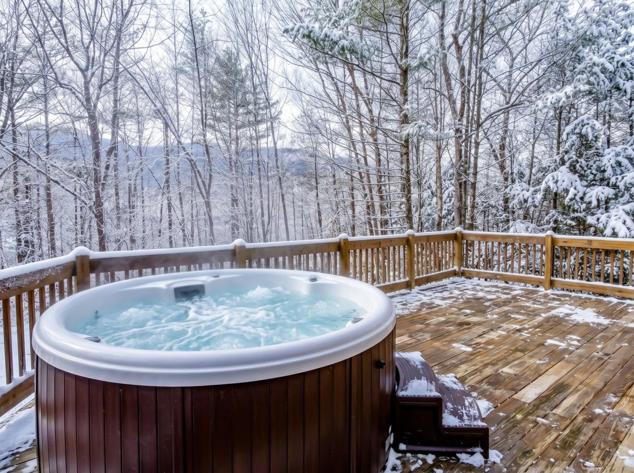 A hot tub on a wooden deck with snow-covered trees in the background.