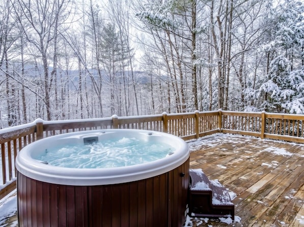 A hot tub on a wooden deck with snow-covered trees in the background.