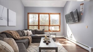 Una sala de estar moderna con un sofá modular, una mesa de centro y un ventanal con vistas a árboles.