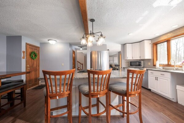A spacious kitchen with wooden chairs, a dining table, and a modern chandelier.