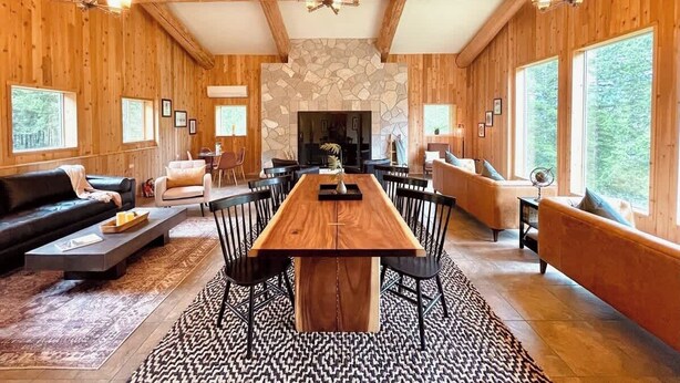 Un salón amplio con una gran mesa de madera para comer, sillas negras y una chimenea.