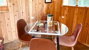 Una habitación con paneles de madera, una mesa redonda de vidrio, dos sillas marrones y cuadros en la pared.