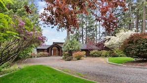 A house with a gravel driveway, surrounded by lush greenery and trees.