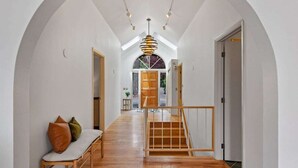A hallway with wooden flooring, a bench with cushions, a staircase, and a ceiling light fixture.