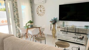 Una sala de estar moderna con un sofá, una mesa de comedor con sillas, un televisor y un jarrón decorativo.