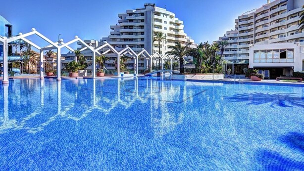 Una piscina con estructuras blancas a su alrededor, rodeada de edificios de varios pisos.