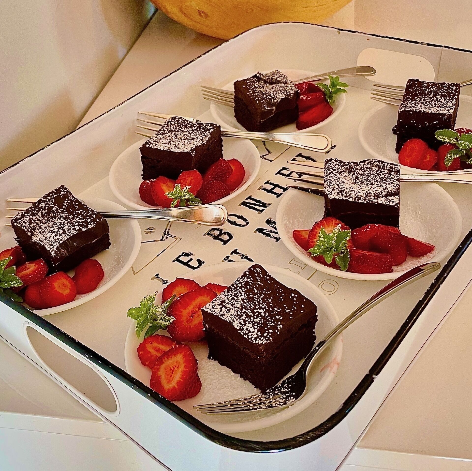 Una bandeja de brownies con fresas sobre una mesa blanca.