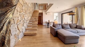 Una sala moderna con pared de piedra, escalera de madera y sofá modular.