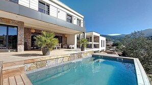 Una casa moderna de dos pisos con piscina, fachada de piedra y vistas a montañas.