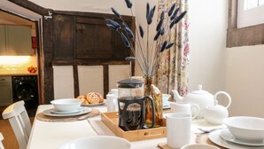 Une table à manger dressée avec de la vaisselle blanche, une machine à café, des théières et un vase contenant des fleurs séchées.