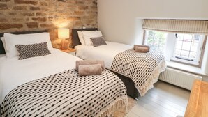 Une chambre avec deux lits, un mur en pierre, une fenêtre avec des rideaux et un plancher en bois.