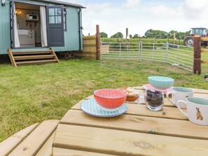 Une table en bois, préparée pour un pique-nique, avec un saladier, une tasse et un petit gâteau.