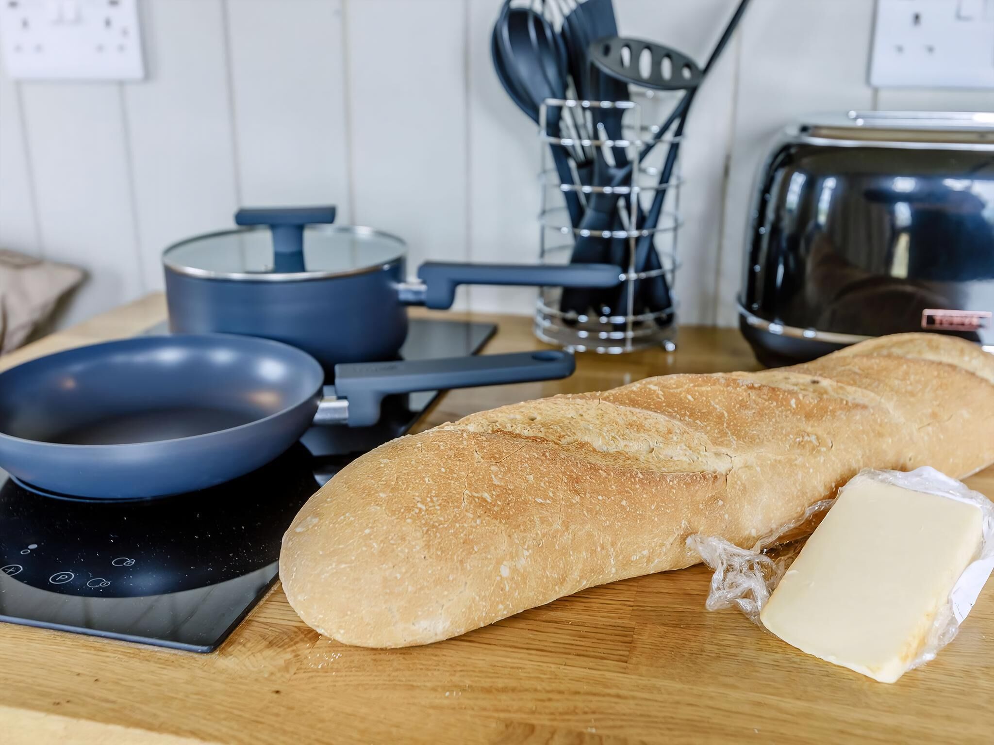 Une cuisine avec un pain, une poêle, une casserole et un grille-pain posés sur un plan de travail en bois.