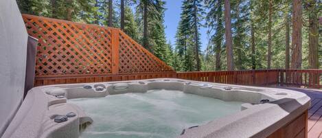 A hot tub on a wooden deck surrounded by tall trees.