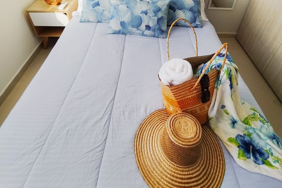 A neatly made bed with a tufted headboard, a basket with a towel, and a woven hat on the bed.