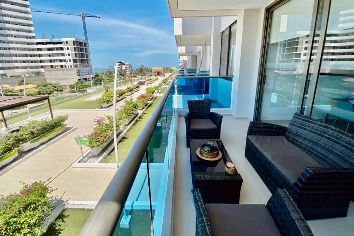 A balcony with a view of a construction site, a modern building, and a landscaped area with plants.