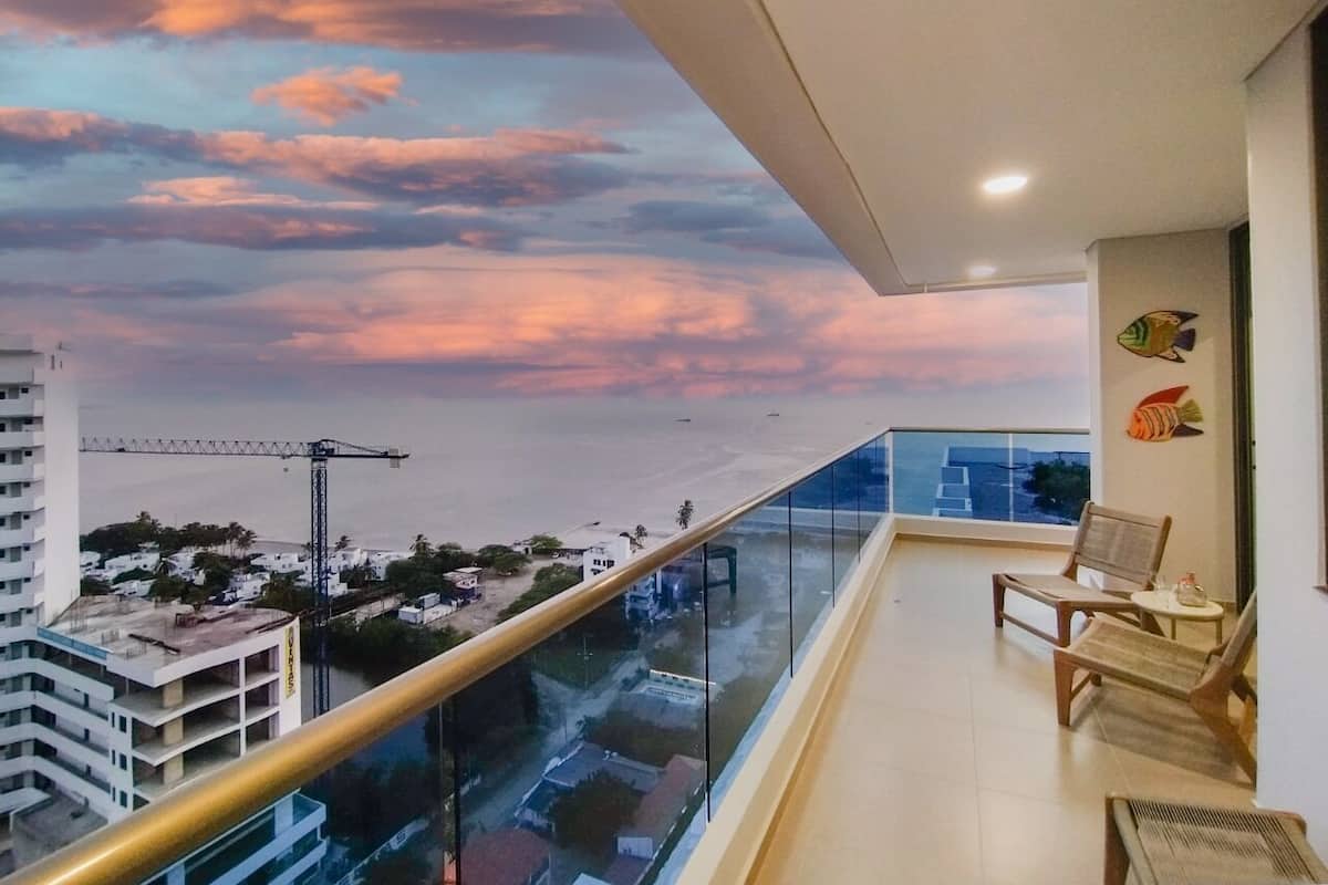 A balcony with a glass railing overlooking a cityscape and a sunset.