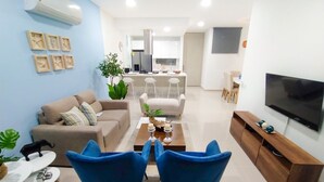 Un salon moderne avec un canapé, deux fauteuils bleus, une table basse et un téléviseur.