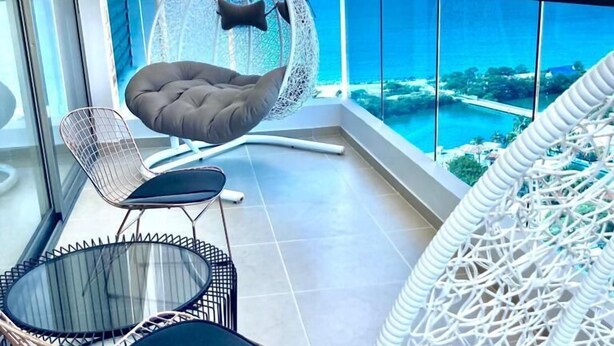 Un balcon avec un fauteuil suspendu, deux chaises et un canapé en osier blanc.