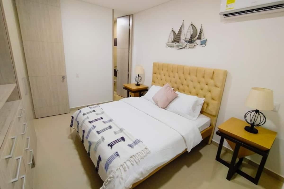 A bedroom with a bed, a nightstand, a wall-mounted air conditioner, and a door.