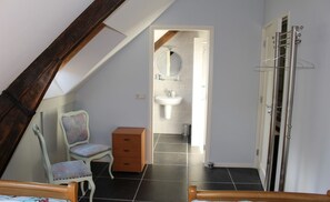 Cozy loft-style room with a single bed, wooden chest, and compact bathroom area.