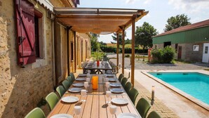 An outdoor dining area with a long wooden table set for a meal, surrounded by chairs, with a pool in the background. - So Villa Noé Michel (72) - Heated pool - Basketball - 2h Paris - 30 p. (Vallon-sur-Gée)