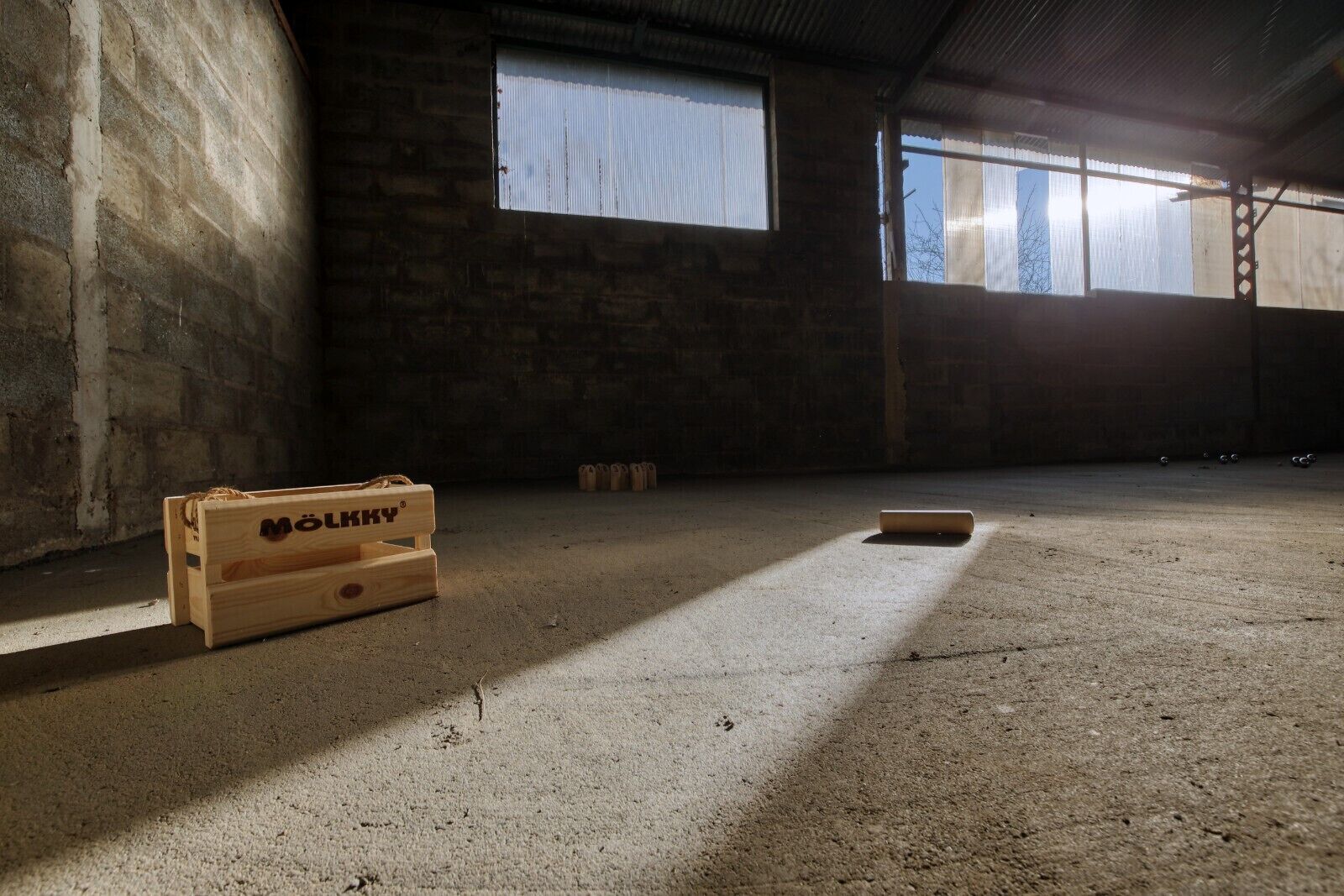 A spacious industrial room with concrete floors and walls, a wooden crate labeled "MOLKKY", and a window allowing natural light.