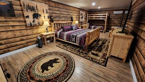 A log cabin-style bedroom with a bed, nightstands, a lamp, a fireplace, and a rug with a bear design. - Cabin Apt 20min to Gatlinburg across from Ntl Park GameRoom+FirePit+Pet Friendly (Cosby)
