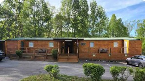 A wooden cabin with a green roof, a front porch, and a parking area. - Cabin Apt 20min to Gatlinburg across from Ntl Park GameRoom+FirePit+Pet Friendly (Cosby)