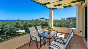 A balcony with a table and chairs, a glass-top table, and a view of the sea and buildings. - Villa Ilos by Villa Plus (Pyrgos Psilonerou)