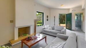 A modern living room with a fireplace, a sofa, a coffee table, and a glass door leading to a shower area. - Villa Ilos by Villa Plus (Pyrgos Psilonerou)