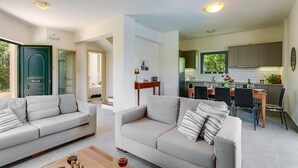 A modern living room with two sofas and a coffee table, a kitchen with a dining area, and a green door. - Villa Ilos by Villa Plus (Pyrgos Psilonerou)