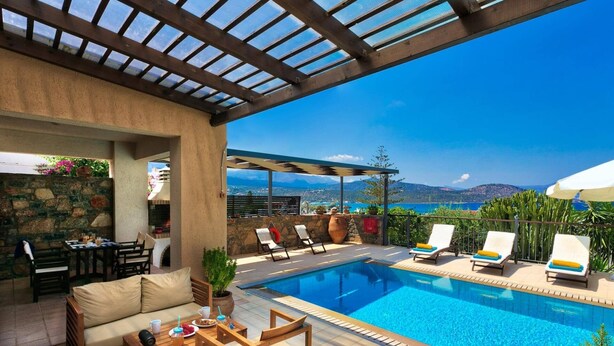 A poolside area with a stone wall, a grill, lounge chairs, and a view of the sea and mountains. - Villa Kallisto by Villa Plus (Istro)