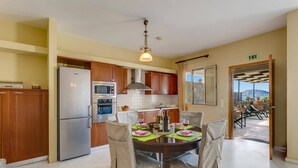 A modern kitchen with wooden cabinets, a built-in oven, and a refrigerator. There is a dining table with chairs and a chandelier above. - Villa Kallisto by Villa Plus (Istro)