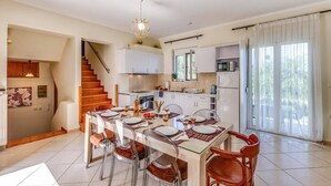Una cucina moderna con mobili bianchi, un'area pranzo con tavolo in vetro e una scala che conduce a un altro piano.