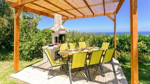 Una veranda esterna con una pergola in legno, un barbecue e un tavolo apparecchiato per mangiare.