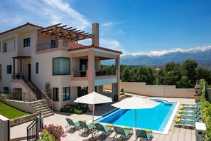A multi-story building with a swimming pool, outdoor seating, and a mountain view.