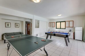 Ein Raum mit Tischtennisplatte, Billardtisch, einer Couch und einer Küchenzeile.