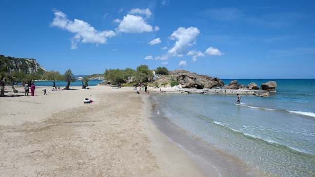 Une plage avec un ciel dégagé, des affleurements rocheux et une eau calme.