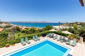 A swimming pool with lounge chairs and umbrellas, overlooking a coastal town and the sea. - Villa Katerina Pente by Villa Plus (Kalives)