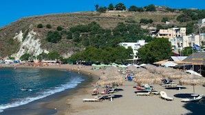 Une plage avec des transats et des parasols, un ciel dégagé et des bâtiments en arrière-plan.
