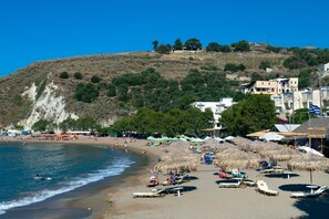 Ein Strand mit Liegestühlen und Sonnenschirmen, ein klarer Himmel und Gebäude im Hintergrund.