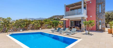 Una casa moderna de dos pisos con piscina, mobiliario exterior y fachada de piedra.