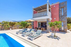 A two-story building with a pool, lounge chairs, and a dining area. - Villa Kery by Villa Plus (Hersonissos)