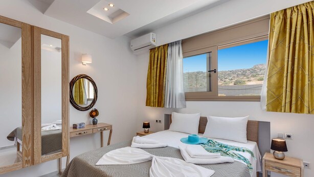Habitación de hotel con cama, mesita de noche, espejo y ventana con cortinas.