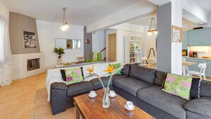 Sala de estar con sofá, una mesa de centro y chimenea. Hay una zona de comedor con mesa y sillas, y una cocina con armarios y encimera.