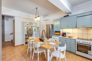 A compact kitchen with a dining table, chairs, a refrigerator, a stove, and a bookshelf.